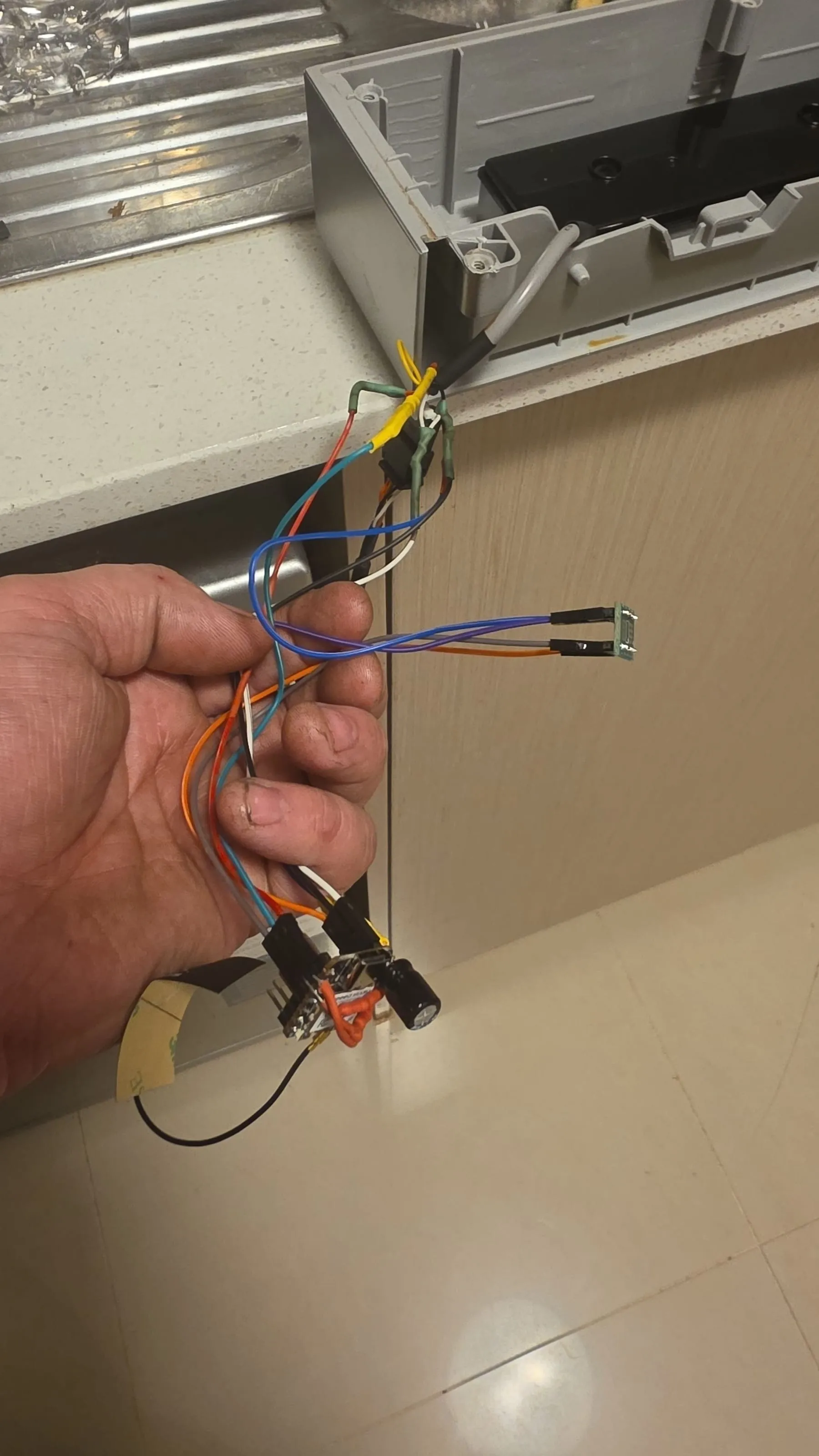 The ESP32 bridge on its wiring loom, held up beside the open dishwasher door, with the panel lead joined in with heatshrink