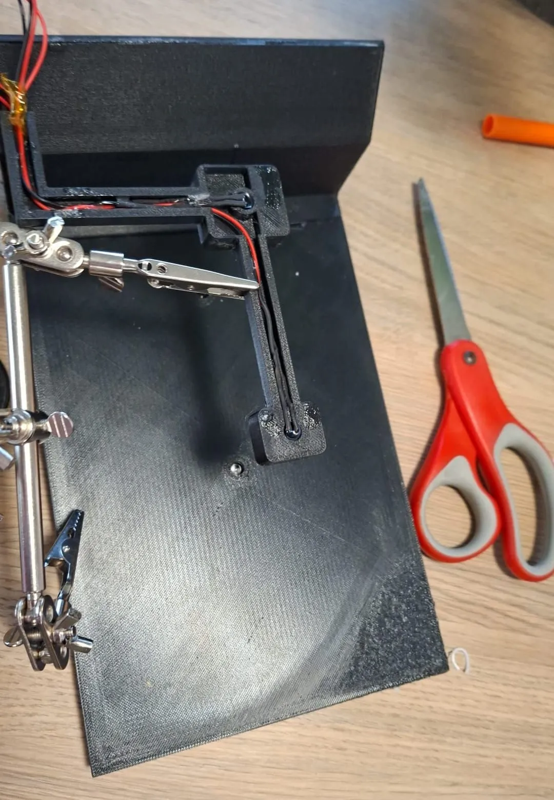 The black 3D-printed false-floor insert upside down on a desk, with red and black wires laid in a printed channel that runs across the underside and up to the bay
