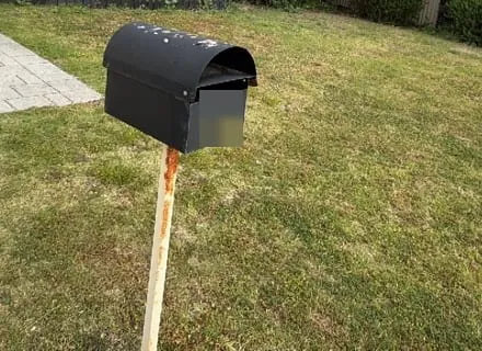 A black steel letterbox on a post on a front lawn, with a curved lid over the slot